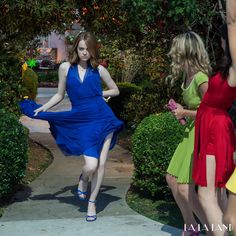 a woman in a blue dress is walking down the sidewalk with other women behind her