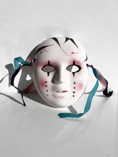 a white mask with red and black markings on it's face, tied to a blue ribbon