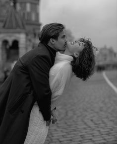 a man and woman kissing in front of a building on a cobblestone street