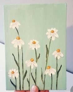 someone is holding up a painting with daisies on it