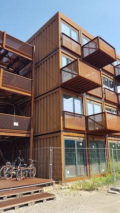 two bicycles are parked in front of an apartment building made out of shipping containers and wooden balconies