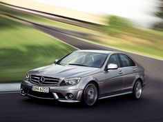 a mercedes c - class driving on a road with blurry grass in the background