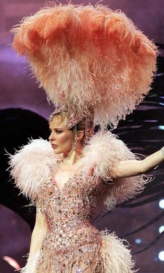 a woman in a feathered dress and headdress walks down the catwalk