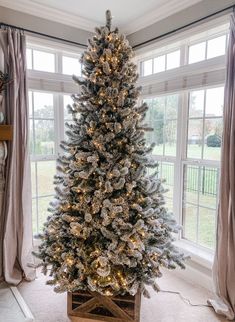 a white christmas tree in a wooden crate with lights on the top and windows behind it