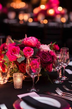 the table is set with wine glasses and pink flowers in vases, candles and napkins