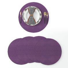 purple placemats and plates on white background with fork, knife and spoon rest next to each other