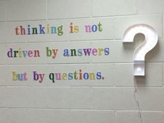 a white light bulb sitting on top of a wall next to a sign that says, thinking is not driven by answers but by questions