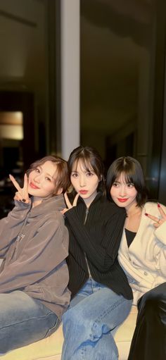 three women sitting on top of a couch with their hands in the shape of two fingers