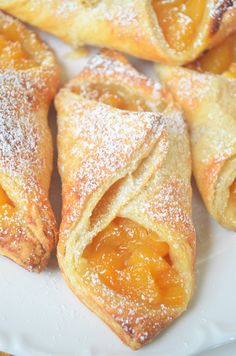 several pastries on a white plate with powdered sugar and oranges in the background