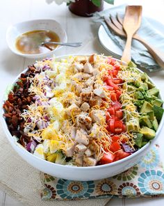 a large salad with chicken, tomatoes, lettuce and other toppings in a white bowl