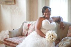 a woman in a wedding dress sitting on a couch smiling at the camera while holding a bouquet