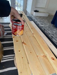 a person holding a can of paint on top of a wooden table next to a dog