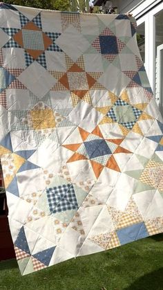 a large quilt is hanging from a clothes line outside on the grass in front of a house