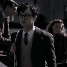 a young man wearing glasses and a tie walking down the street with other people behind him