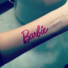 a woman's arm with the word barbie written on it and a cup in the background