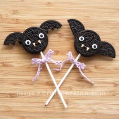 two cookies shaped like bats with eyes and bows on them are sitting on a wooden surface