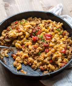 a skillet filled with macaroni and cheese on top of a wooden table