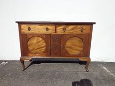 an old wooden cabinet with two doors and knobs on the front, sitting in a parking lot