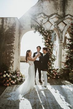 a newly married couple standing in front of an arch with flowers on it and holding hands