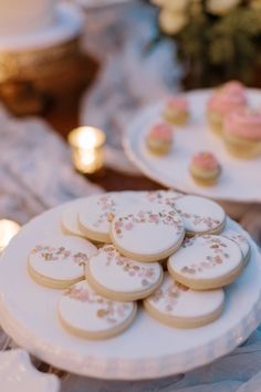 some cookies are sitting on white plates with pink frosting and sprinkles