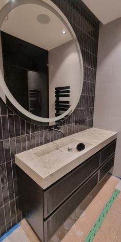 a bathroom vanity with a round mirror above it and tile on the wall behind it