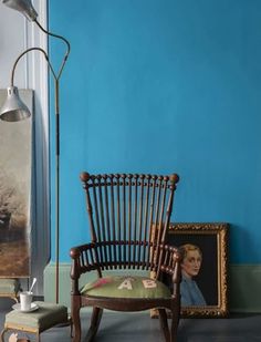 a chair sitting in front of a blue wall next to a lamp and pictures on the floor