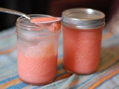 two jars filled with liquid sitting on top of a striped table cloth next to a spoon