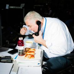 a man sitting at a desk eating pizza and talking on the phone