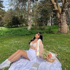 a woman sitting on top of a blanket in the grass next to a basket filled with flowers