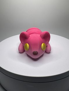 a pink toy with yellow eyes sitting on top of a white table next to a round object