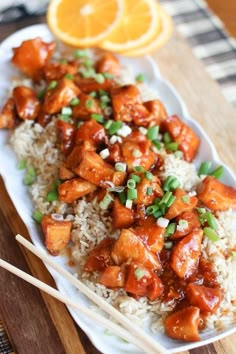 a white plate topped with chicken and rice next to chopsticks on a wooden table