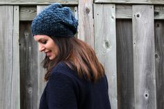 a woman wearing a blue knitted hat standing in front of a fence with her eyes closed