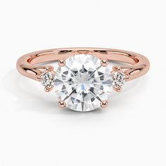 a rose gold engagement ring with two diamonds on the band and a round cut diamond in the center