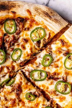 a pizza with cheese, green peppers and meat on it sitting on a marble counter top