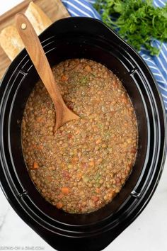 a wooden spoon in a black crock pot filled with lentils and carrots