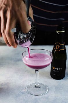 a person pours a drink into a wine glass with a pink substance in it