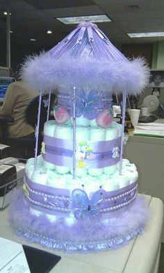 a baby shower cake with purple feathers and diapers on it's sides, sitting on a desk in an office cubicle