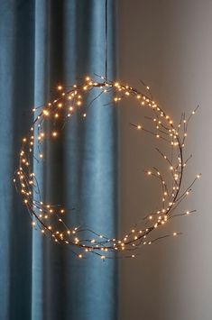 a wreath with lights hanging from it's sides in front of a blue curtain