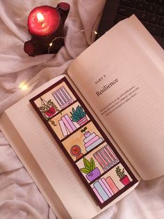 an open book sitting on top of a bed next to a computer keyboard and candle