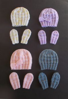 six knitted hats and mittens laid out on a black surface, all in pastel colors