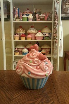 a cupcake with pink frosting sitting on top of a wooden table next to shelves