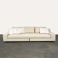 a white couch sitting on top of a cement floor next to a wall with two pillows