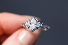 a woman's hand holding an engagement ring with blue and white diamonds on it