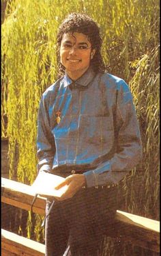 a young man sitting on a bench in front of tall grass