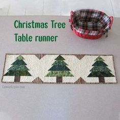 a christmas tree table runner is on the floor next to a red basket and bowl