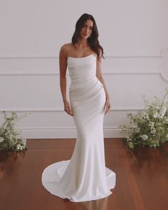 a woman in a white dress standing on a wooden floor next to flowers and greenery