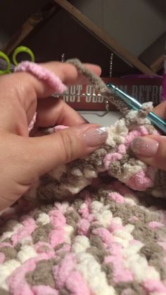 two hands crocheting together on a blanket with scissors and yarn in the background