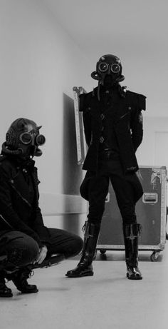 two people in gas masks are sitting on the floor and one person is wearing a suit