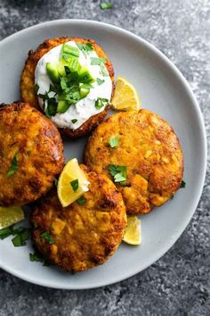 three crab cakes on a white plate with lemon wedges and sour cream in the middle