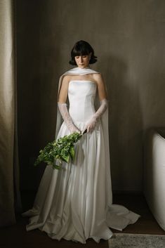 a woman in a white wedding dress holding a green plant with gloves on her hands